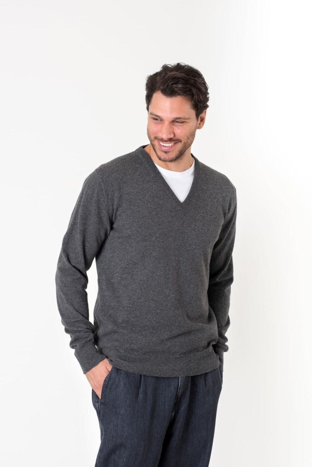 Uomo sorridente indossa un maglione grigio scuro con scollatura a V, su sfondo bianco. Look casual e moderno.